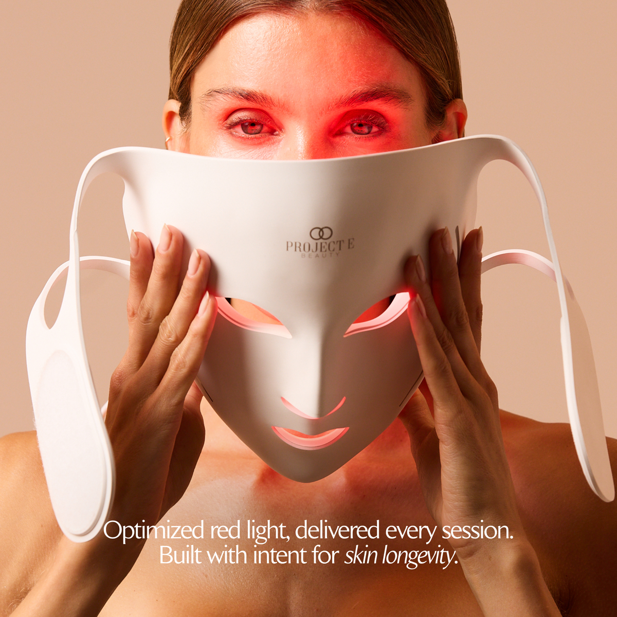 Woman holding the white LumaLux Face V2 mask in front of her face with red light visible behind it