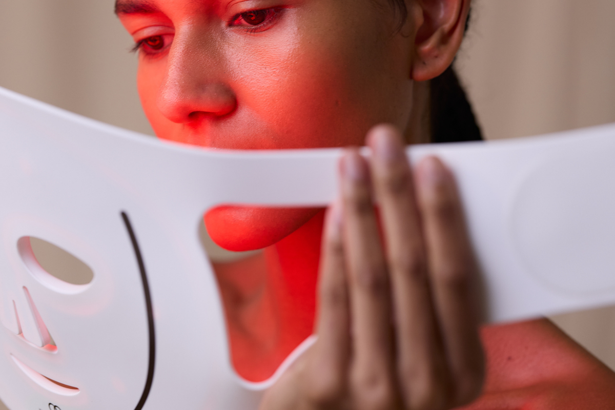 Model holding LumaLux Face Pro LED red light therapy mask showing glowing red and infrared LEDs.
