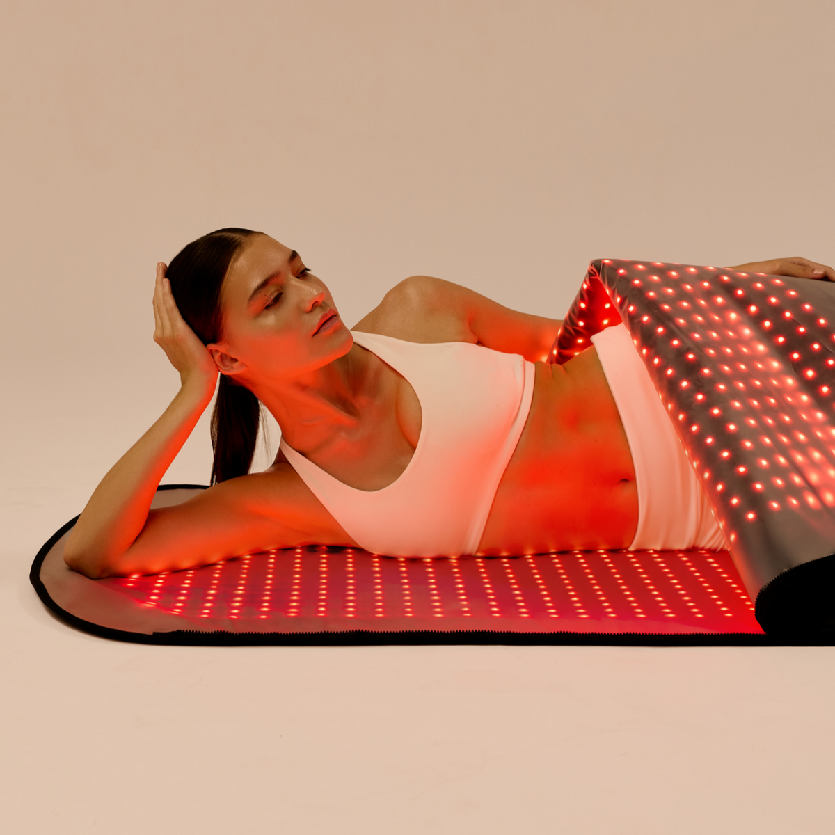 Woman reclining on the illuminated lower Restora+ LED mat while lifting the upper panel