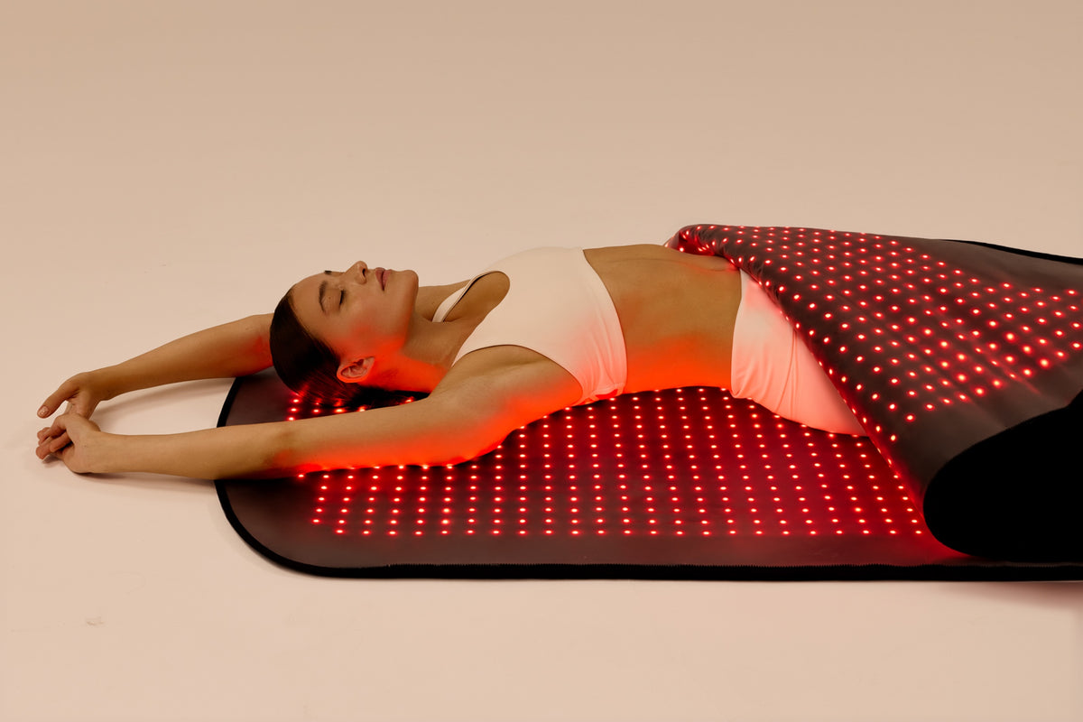 Woman lying on the Restora red light therapy mat with the LEDs on